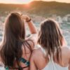 photo of two young women looking out over city with sun setting behind hills