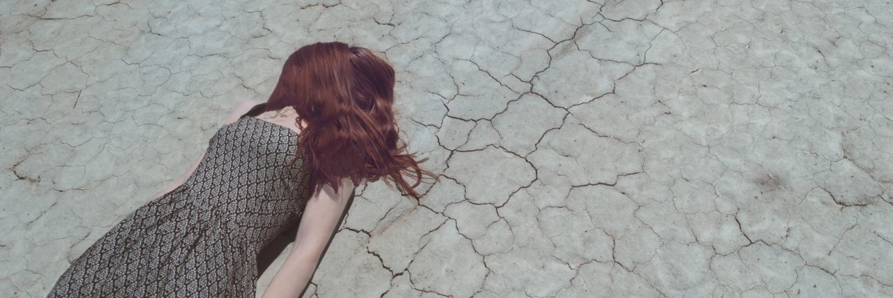 photo of redhead woman lying on cracked ground face down