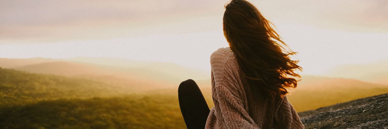 photo of young woman relaxing and looking at sunset over hills