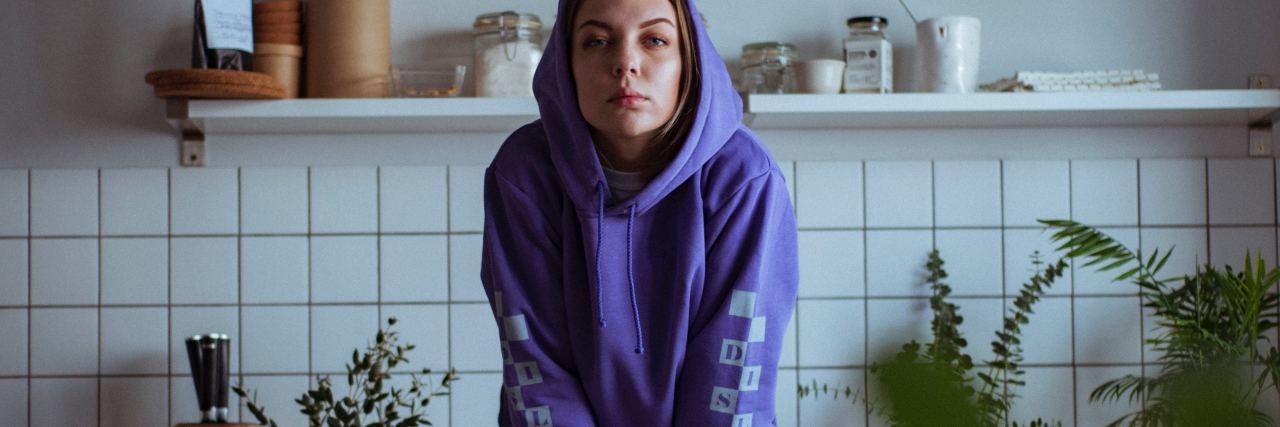 photo of woman wearing purple hoodie sitting on countertop and looking into camera