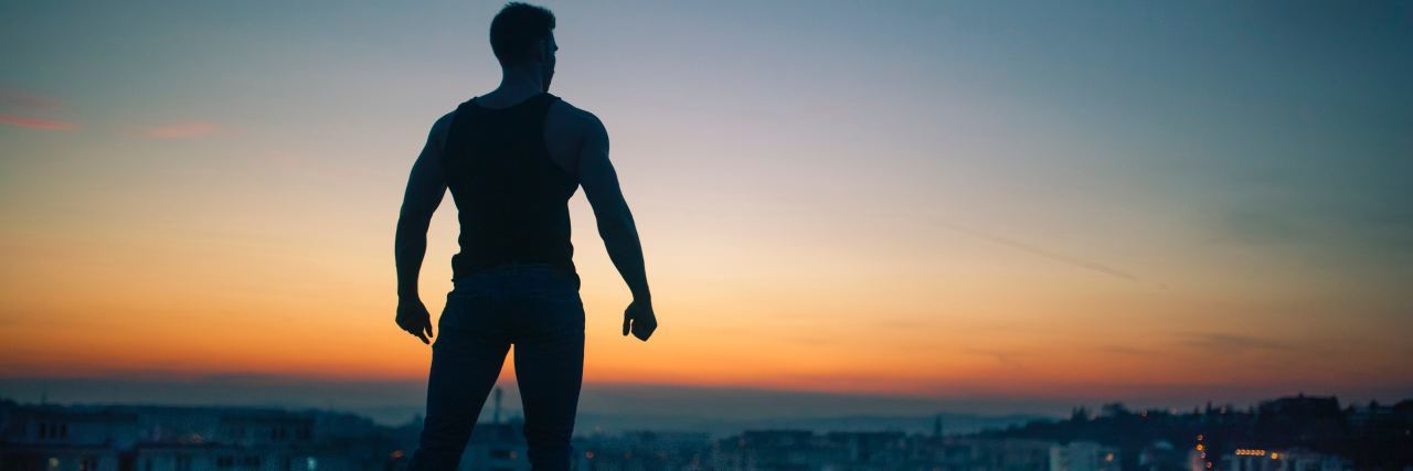 The Positive Parts of Having a Chronic or Mental Illness photo of man silhouetted against sunset sky in superhero pose, fists clenched and confident, looking out over city