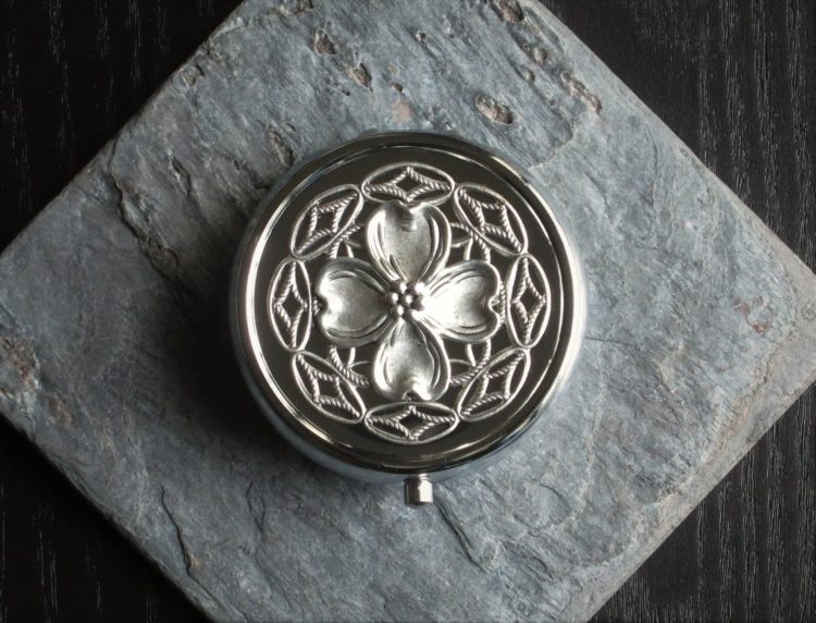 A silver pill box with a flower on top of it.
