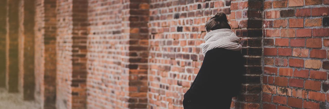 photo of woman standing by brick wall facing away