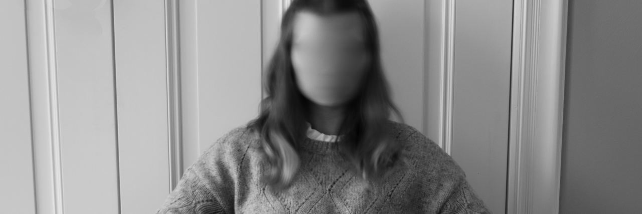 black and white photo of woman sitting on chair with legs crossed and face blurred