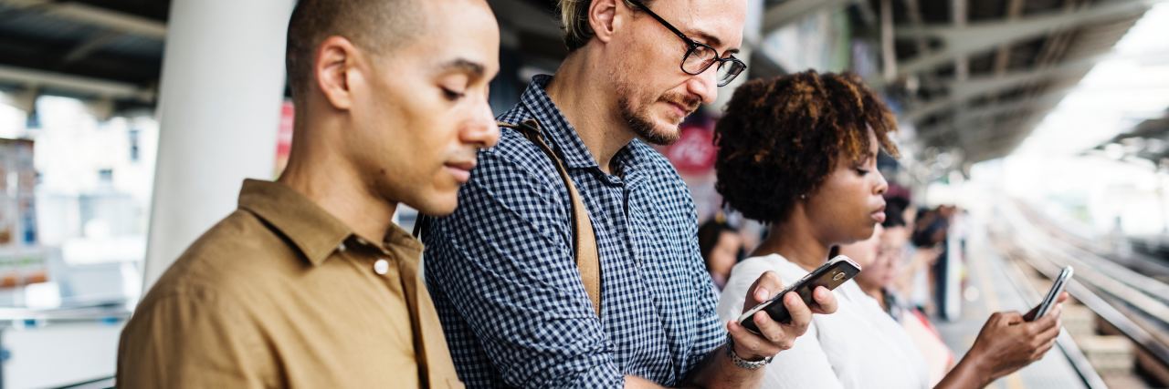 people with smartphones standing together while waiting on a train