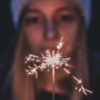 close up photo of blonde woman wearing hat and looking at sparkler