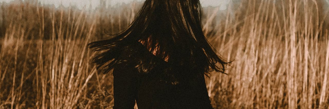 What to Know About Living With an Invisible Illness photo of woman standing in field with hair hiding face
