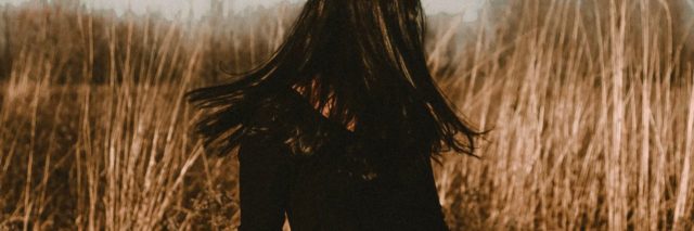 photo of woman standing in field with hair hiding face