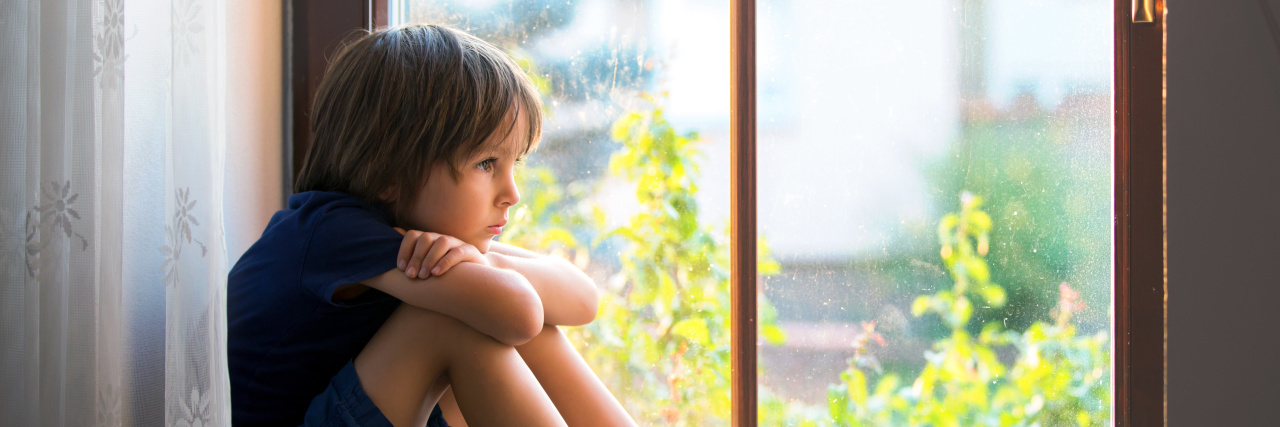 Sad child, boy, sitting on a window sill