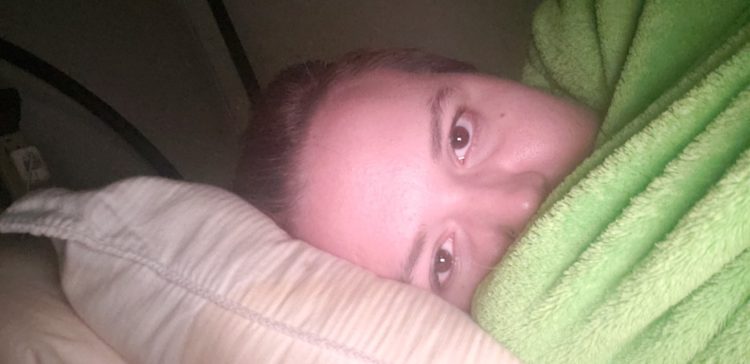 A photo of a young woman laying in bed, without makeup.