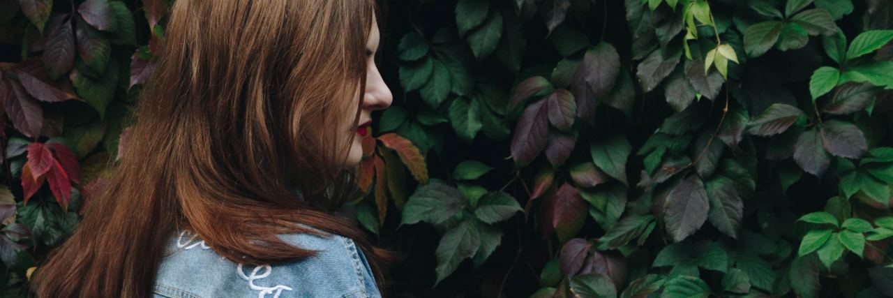 What to Do When Anxiety Says Something Bad Might Happen photo of woman with red hair standing in front of bush wearing denim jacket