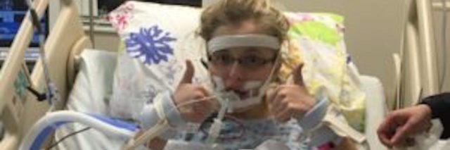 The author in a hospital bed with her thumbs up
