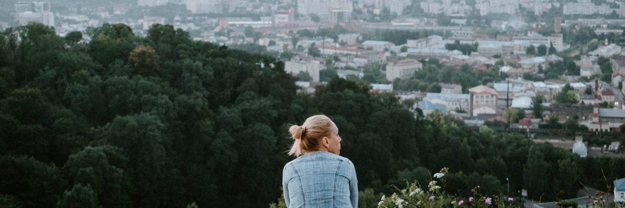 photo of young woman standing alone looking out over city