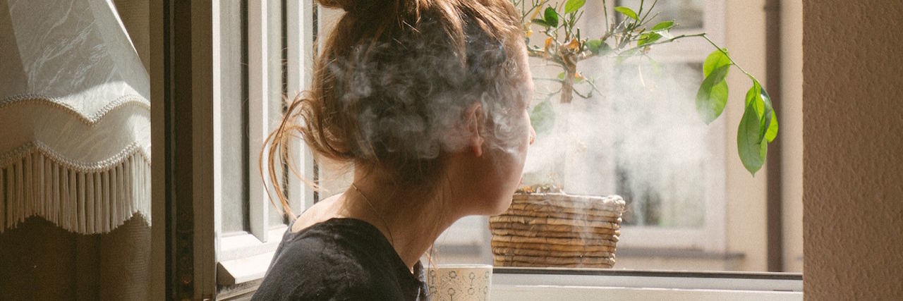 A woman looking out the window smoking a cirgarette
