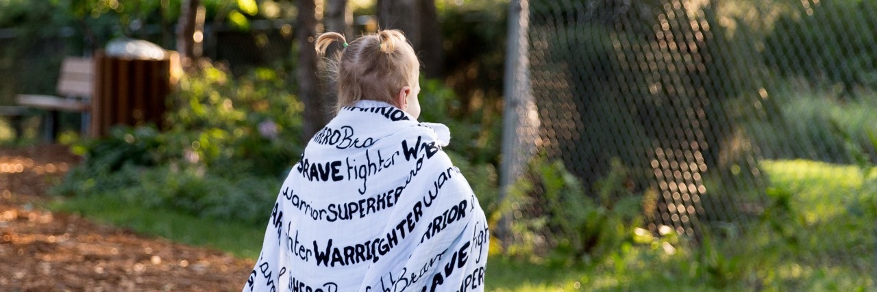 The Brave Face I Wear as a Mama to a Child With a Disability a little girl wrapped in an inspirational blanket