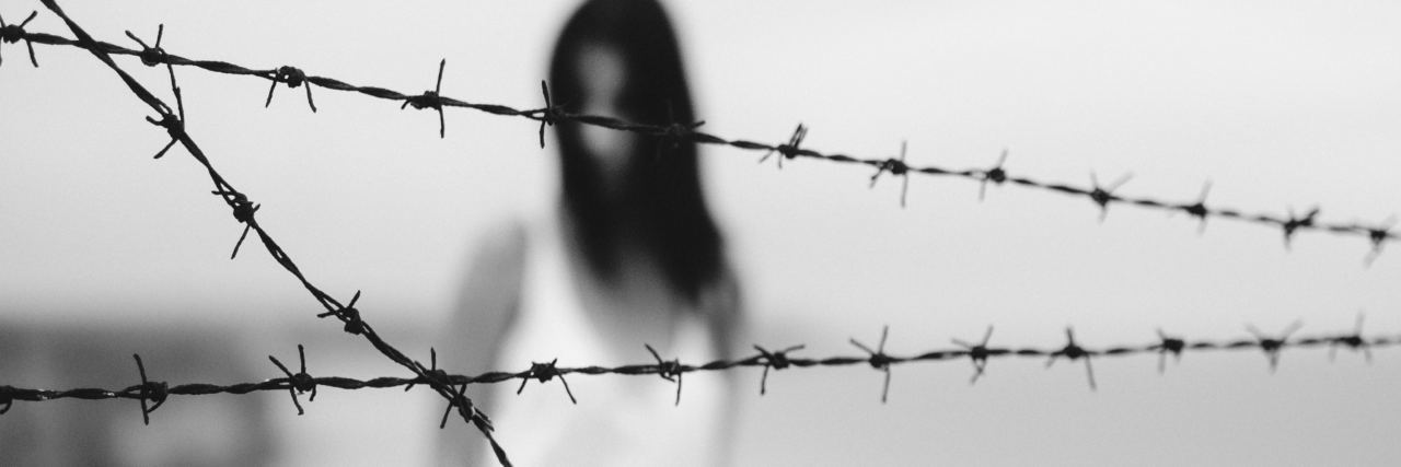 blurred black and white photo of silhouetted woman with crossed barbed wire in focus in foreground