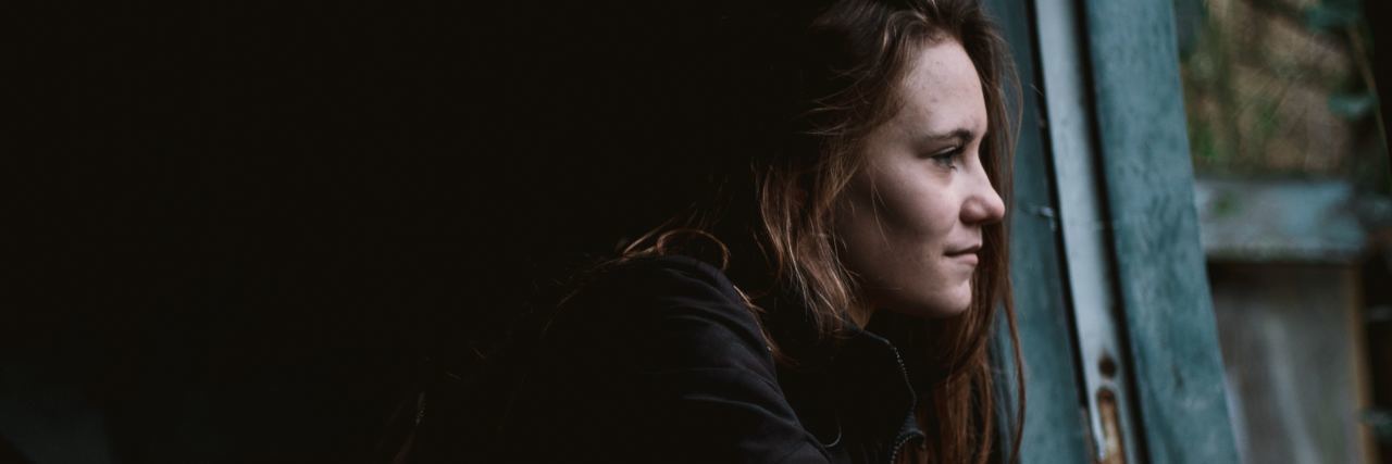 How to Combat Shame and Perfectionism for Mental Health profile photo of woman looking out of window in dark house and smiling