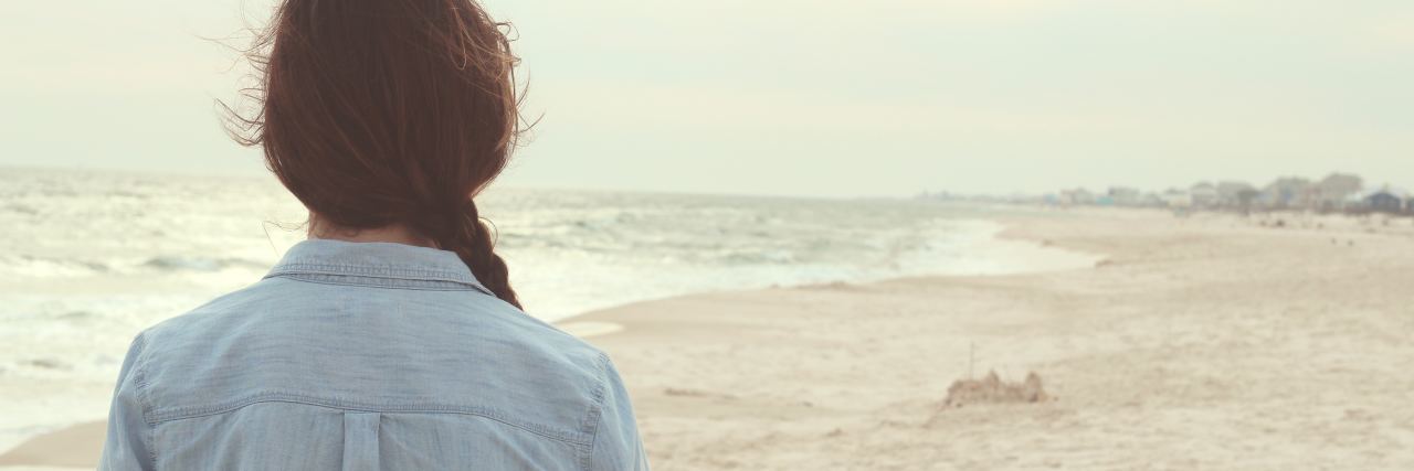 How to Understand Fear of Abandonment With BPD photo of woman standing on empty beach looking out over sand and waves