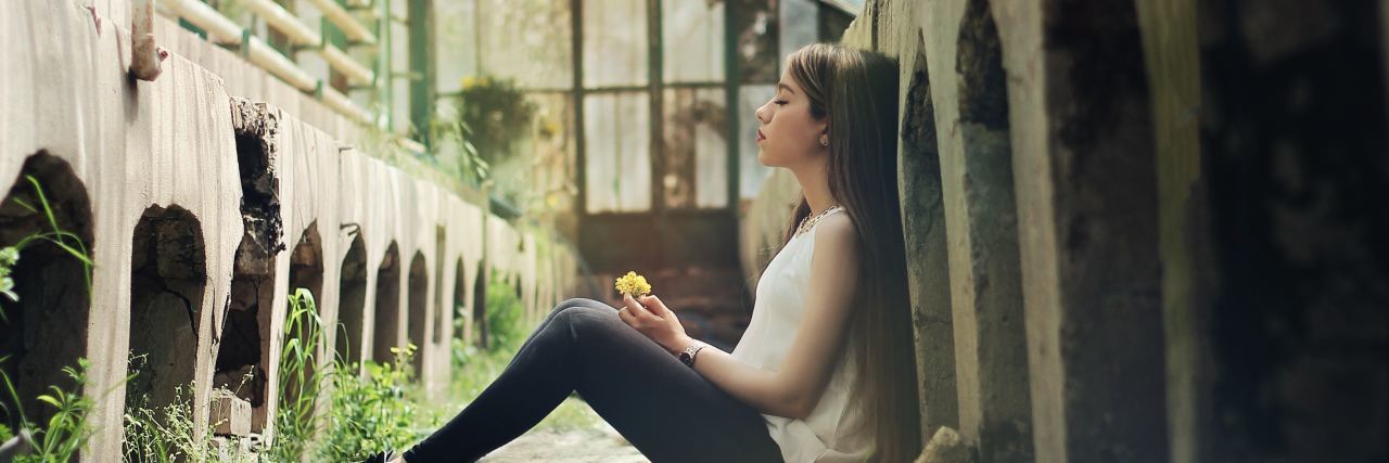 young woman sitting in abandoned building holding flower
