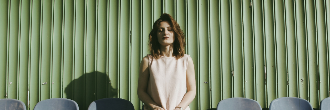 11 'Habits' of People Who Grew Up With Emotionally Absent Fathers A woman sits alone among empty seats, her hands rest on her knees, and her eyes are closed in calm. Beneath her reads: 11 'Habits' of People Who Grew Up With Emotionally Absent Fathers.