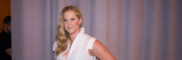 Amy Schumer boses while wearing a white and navy outfit