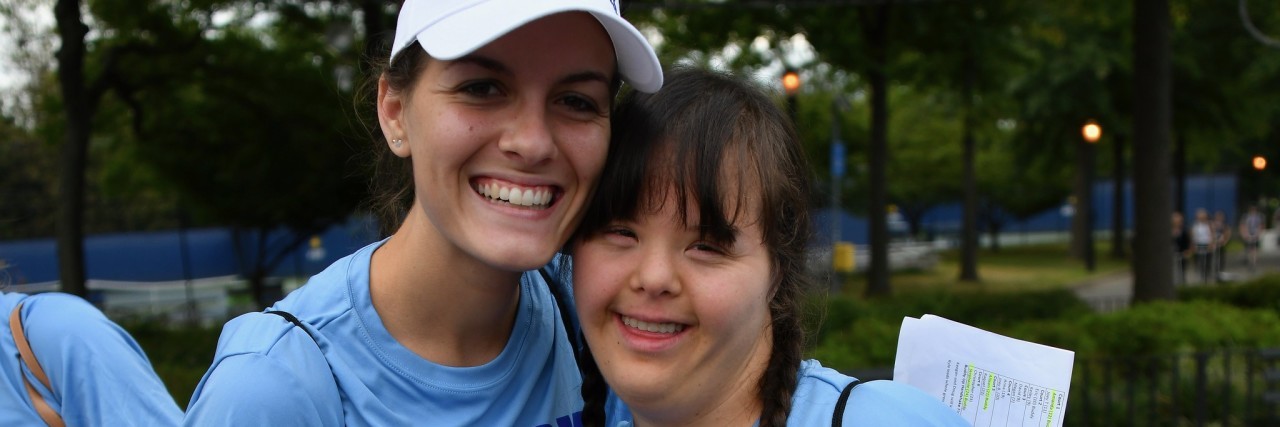 Two women wearing matching blue shirts smiling at camera, one woman has Down syndrome