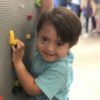 Boy with Down syndrome looking at camera while holding on to lego pieces on a lego board wall.