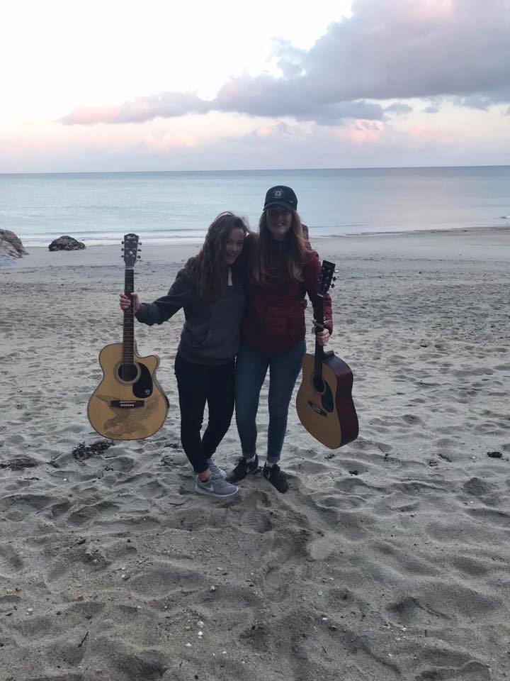 women standing on a beach. one woman's legs are bending and curving due to hyperextension from ehlers-danlos syndrome