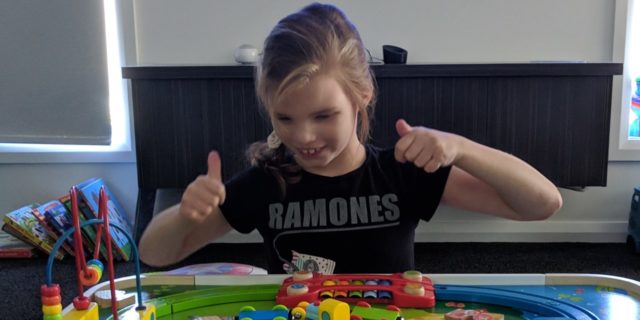 A little girl is giving a thumbs up while playing.