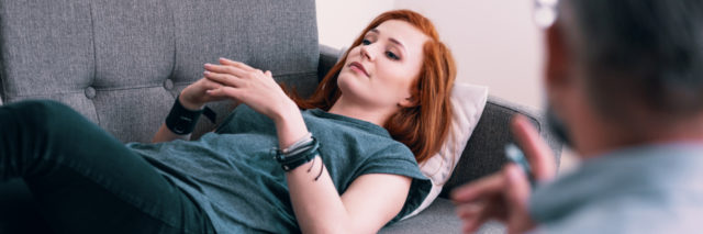 young woman lying on a gray couch in psychologist's office. Coping with loss concept. Blurred therapist in the foreground