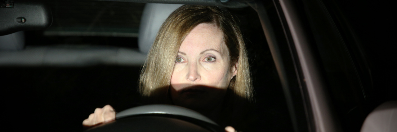 How I Connect to Music on Drives Home With My Chronically Ill Child a woman is in a car behind the wheel with headlights shining in her face