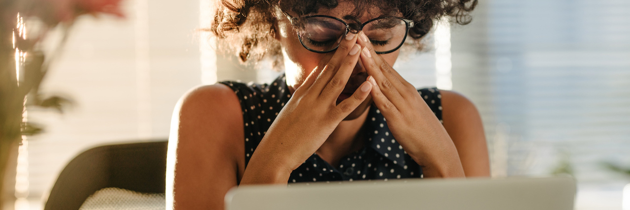 What to Remember When Bad News Makes You Feel Hopeless A woman sitting a her computer, with her hand covering her eyes. She looks frustrated.