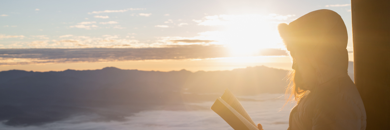 Bible Verses for When You Struggle With Body Image a woman is holding a bible and reading it overlooking a mountain
