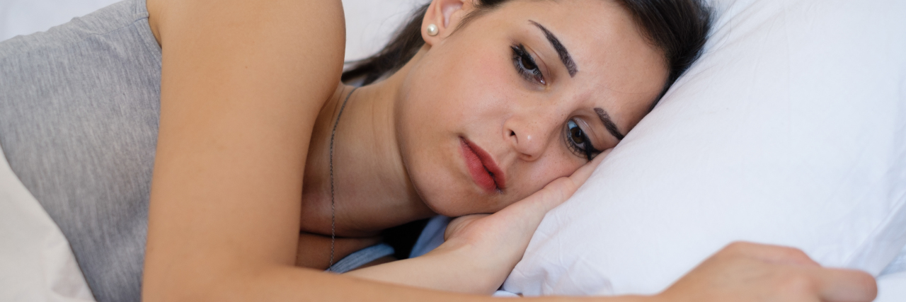 Navigating the Daily, Gut-Wrenching Reminders of Infertility a young sic woman lying in bed