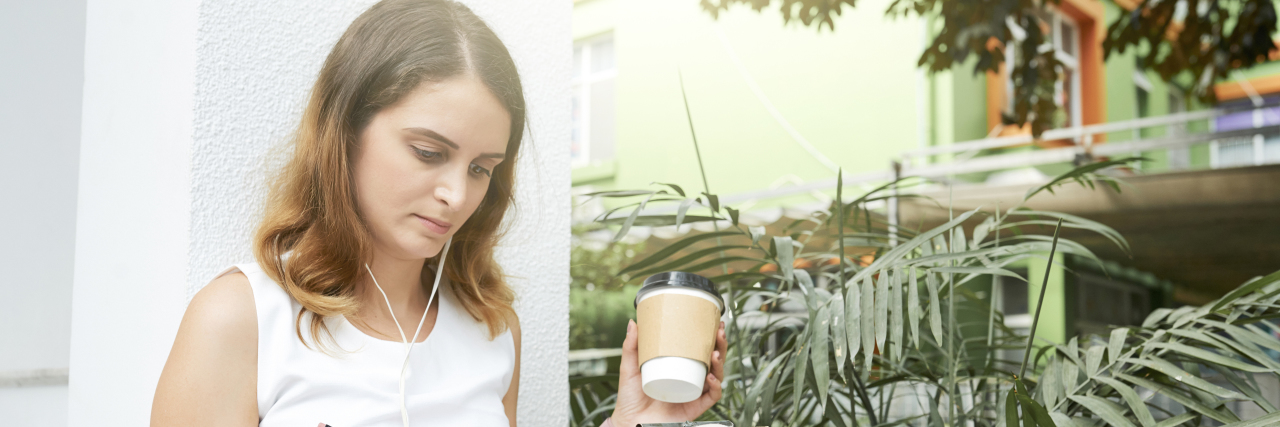 young woman taking notes and drinking coffee with earbuds on