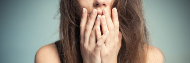 close up photo of woman with long hair and hands raised to her mouth in shock or panic