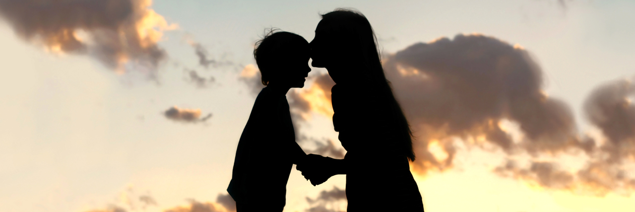 a silhouette of a mom kissing a child on the forehead
