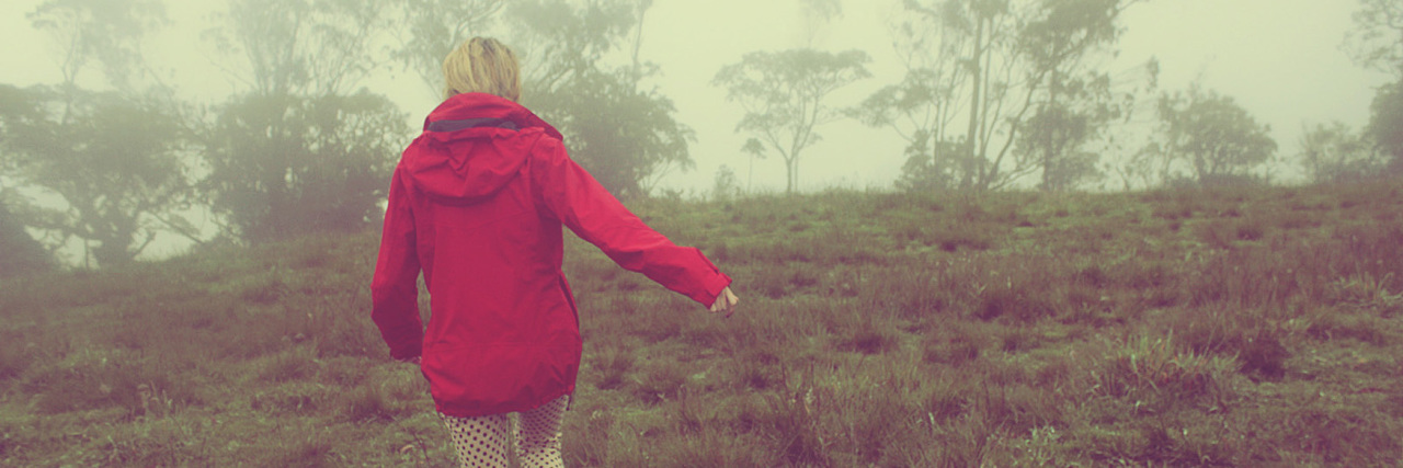 photo of woman with blonde hair and red coat walking through foggy field landscape