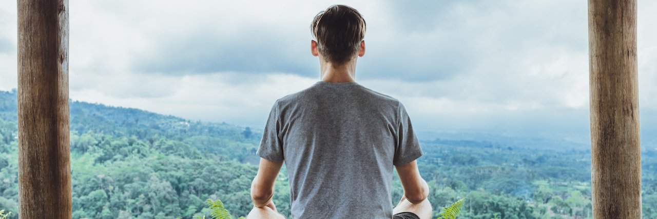 The Limitations of Meditation A man sitting crossed-legged, looking over at a view of trees