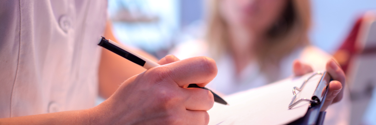 I'm Scared to Admit I'm Taking Antidepressants close up photo of doctor filling in patient notes with patient out of focus in background