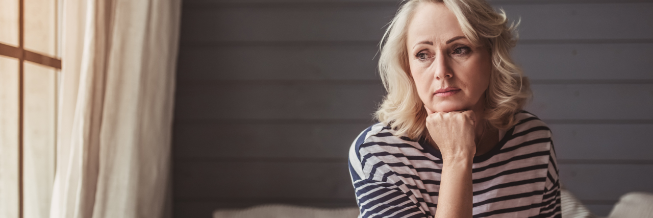 Missing Your Healthy Body After a Chronic Diagnosis woman with head on hand, looking out, sitting on a sofa