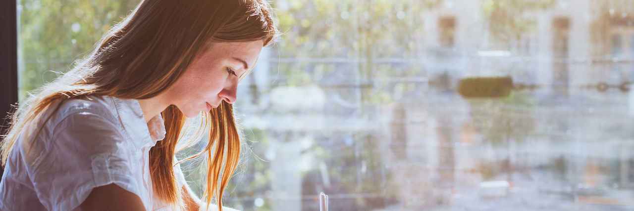 When You Don't Graduate College in 4 Years Because of Your Health A woman writing in a notebook, sitting in front of a window