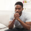 Young african-american man sitting at home. Sad guy sitting on the couch , copy space