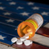 Oxycodone is the generic name for a range of opoid pain killing tablets. Prescription bottle for Oxycodone tablets and pills on wooden USA flag
