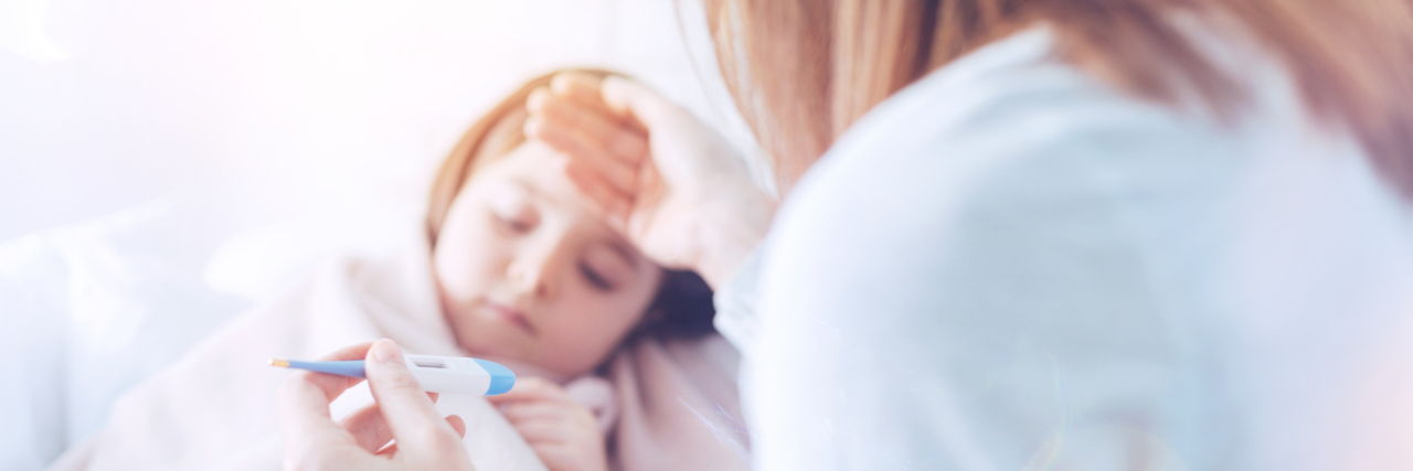 Feeling Guilty When Parenting a Child With a Rare Disease Worried mother putting her right hand on the forehead of her daughter and keeping thermometer in left hand while sitting next to her kid