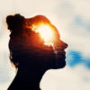 A silhouette of a woman against the sky and clouds and sun