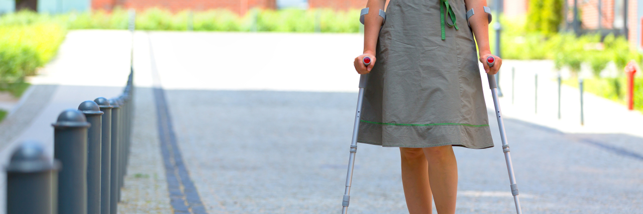 Woman walking with crutches outdoors.