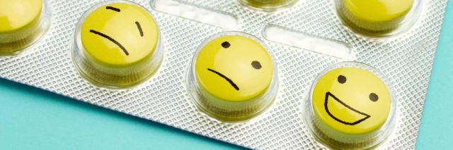 Yellow pills with two sad faces and one happy face on a blue background