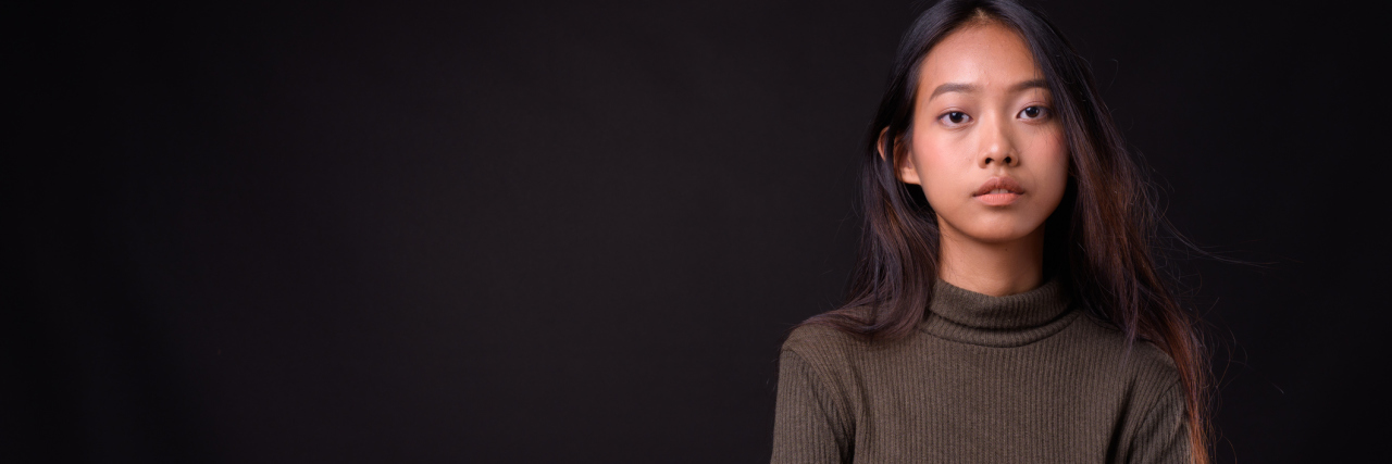 Danish Study Finds Women Are Diagnosed Later Than Men woman crossing her arms and looking serious. she's standing against a black background