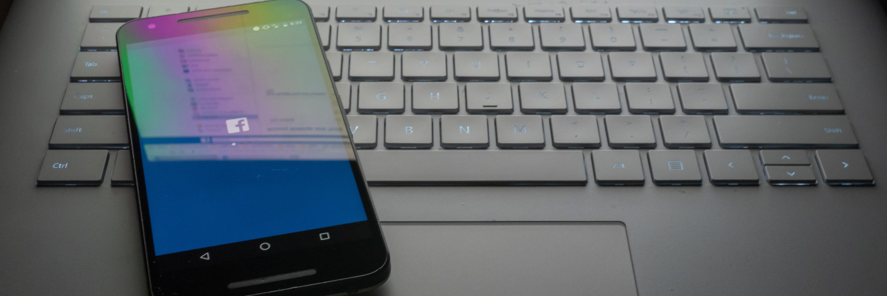 Government Wants to Use Social Media to Decide Disability Benefits Phone sitting on laptop with Facebook icon on screen